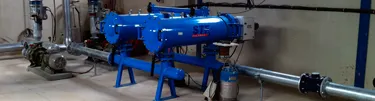 Sala de filtrado con filtros azules automáticos, bombas y tuberías de acero galvanizado.