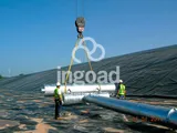 Izado con grúa de un tramo de tubería sobre la lámina impermeable de una balsa, con dos operarios guiando la maniobra.