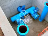 Arqueta de hormigón con una derivación de tubería azul, válvulas y juntas de desmontaje.
