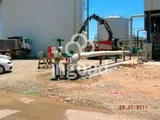 Tubería aérea sobre soportes junto a los tanques de la planta, con un operario trabajando en una conexión.