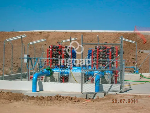 Estación de filtrado vallada al pie de un talud, con baterías de filtros rojos y colectores azules.